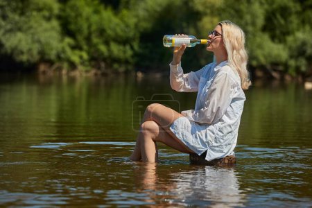 Foto de Mujer joven relajándose en el río con una botella de vino, bebiendo alcohol - Imagen libre de derechos