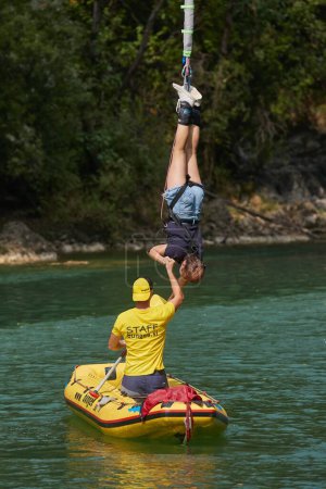 Téléchargez les photos : Solkan, Slovénie - Vers 2022 : Un homme aide une fille à monter dans un bateau sur la rivière lorsqu'elle est suspendue à un cordon élastique après avoir sauté du pont Solkan - en image libre de droit