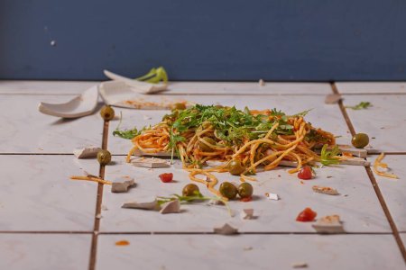 Photo for Plate of spaghetti dropped on the kitchen floor and breaking, dressed with vegetables - Royalty Free Image
