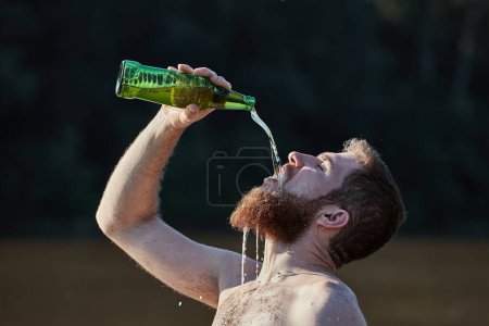 Photo for Bearded man on the beach drinking a bottle of beer pouring from high above like crazy - Royalty Free Image