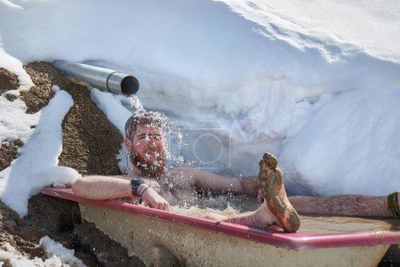 Snowy cold plunge, outdoor cold water immersion in an old bathtub left by a mountain spring in the Alps. Deliberate cold exposure therapy