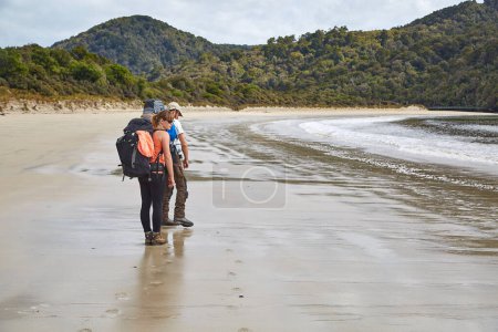 Photo for Man and woman hiking with backpack arriving to sandy beach in New Zealand, Rakiura Stewart Island - Royalty Free Image