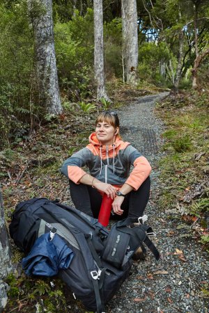 Photo for Woman hiking with backpack in lush green forests of New Zealand, Stewart Island, Rakiura. Sitting down for a rest and drink - Royalty Free Image