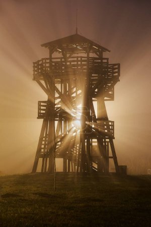 Photo for Wooden lookout tower on a misty night, street lamp light rays flaring through the fog - Royalty Free Image