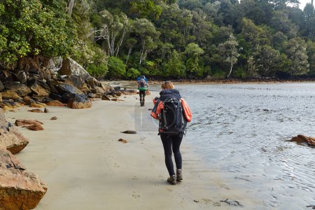 Man and woman hiking with backpack arriving to sandy beach in New Zealand, Rakiura Stewart Island