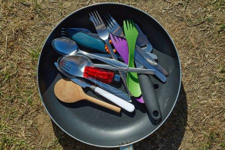 Photo for A pile of kitchen utensils in a pan outdoors in a camping. Forks, spoons, knives, some plastic, some metal, clean washed - Royalty Free Image