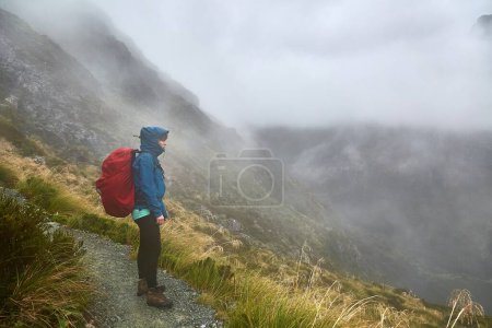 High mountains landscape along the Routeburn Track, Great Walk hiking trail in New Zealand South Island, female hiker standing in foggy weather with backpack