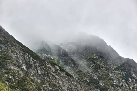High mountain landscape with fog and clouds passing through rough cliffs in the Romanian mountain range Fagaras