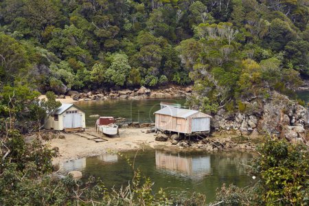 Small harbor in Golden Bay, Oban, New Zealand. Small wooden boathouses, sheds on the rocky shore