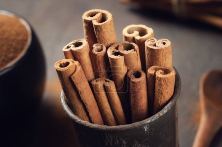 Photo for Cinnamon sticks and bowl of powdered cinnamon on background. Selective focus. - Royalty Free Image