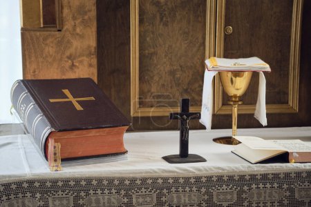 Foto de Composición de símbolos católicos. La Biblia, la cruz de madera y el cáliz dorado en el altar. - Imagen libre de derechos