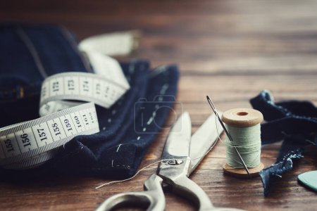 Téléchargez les photos : Un jean raccourci. Ruban à mesurer, ciseaux, bobines de fil et de craie sur table en bois. Coupe de jeans. - en image libre de droit