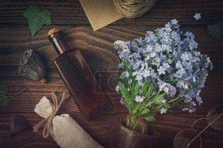 Photo for Tincture or potion bottle, sachet of dried herbs, glasses, bouquet of wild forget me not flowers. Top view, flat lay. - Royalty Free Image