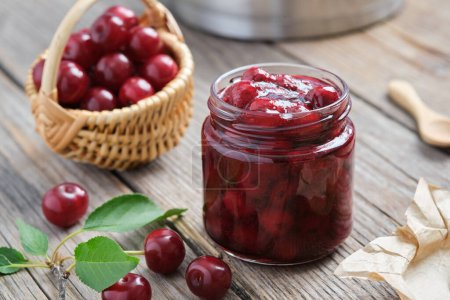Photo for Jar of homemade cherry jam and basket of ripe cherries on kitchen table. - Royalty Free Image