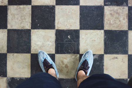 Foto de Hombre con cubiertas de zapatos azules usadas sobre botas de pie sobre baldosas viejas. Piernas en cubiertas de zapatos desechables contra el fondo del piso cubierto con baldosas antiguas. - Imagen libre de derechos