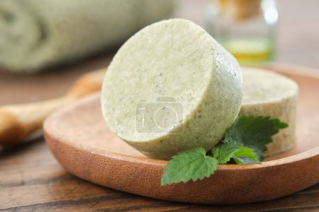 Photo for Nettle solid shampoo pieces or homemade natural organic soap bars on wooden soap dish, fresh green nettle leaves. A bath towel, essential oil bottle and comb on background. Selective focus. - Royalty Free Image