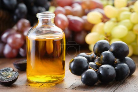 Téléchargez les photos : Graines de raisin bio bouteille d'huile essentielle. Raisins noirs, verts et violets sur la table. - en image libre de droit