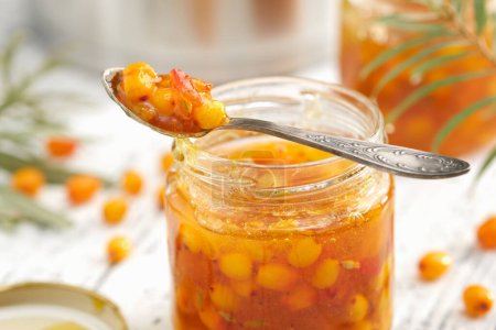 Photo for Jar of healthy sea buckthorn jam. A spoonful of buckthorn jam close up. A pot, jam jar and sea buckthorn berries in the background. - Royalty Free Image