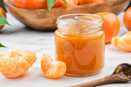 Foto de Tarro de mermelada de mandarina saludable en la mesa de la cocina blanca. Cuenco de madera de mandarina naranjas fruta sobre fondo. - Imagen libre de derechos