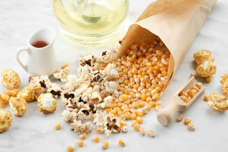 Téléchargez les photos : Popcorn, grains de maïs séchés, sauce caramel et bouteille d'huile sur la table de cuisine. - en image libre de droit