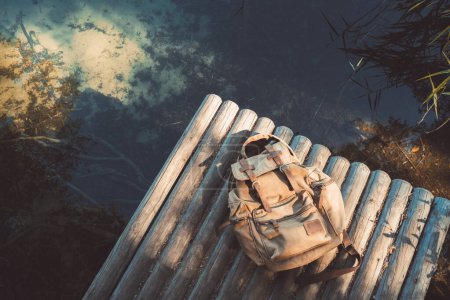 Foto de Mochila de viajero en muelle de madera cerca de lago tranquilo verano. Vista desde arriba. - Imagen libre de derechos