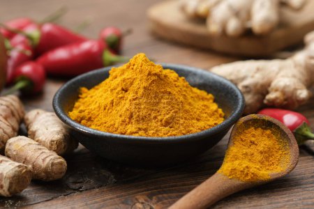 Photo for Bowl of curcuma ground to powder and whole turmeric roots. Red chilli pepper pods and ginger roots on background. Ingredients for cooking and Ayurveda. - Royalty Free Image