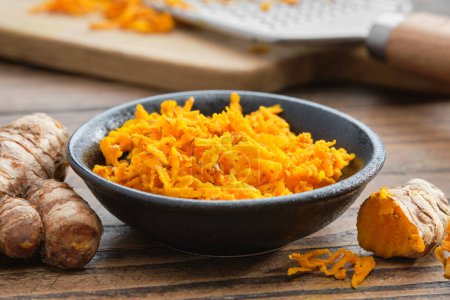 Photo for A bowl of grated fresh turmeric roots. Whole curcuma roots, cutting board and grater on background. Healthy food. - Royalty Free Image