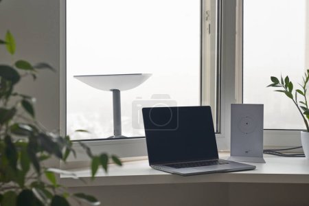 Photo for KYIV, UKRAINE - JANUARY 24, 2023: Starlink antenna behind window with wi-fi router and laptop on windowsill in apartment interior. - Royalty Free Image