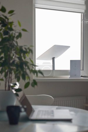 Foto de KYIV, UKRAINE - JANUARY 24, 2023: Starlink antenna and wi-fi router on windowsill in home office interior with laptop on table with cup of coffee in foreground, selective focus. - Imagen libre de derechos
