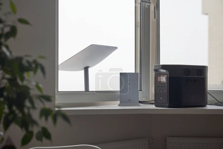 Photo for KYIV, UKRAINE - JANUARY 24, 2023: Starlink antenna behind window, wi-fi router and Ecoflow generator on windowsill in cozy apartment interior. - Royalty Free Image
