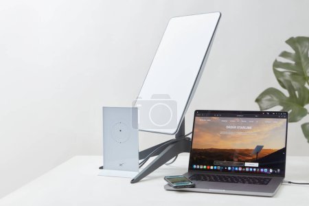 Photo for KYIV, UKRAINE - JANUARY 24, 2023: Starlink antenna, wi-fi router and laptop with Starlink software on display on white desk, houseplant in background. Necessities for remote work. - Royalty Free Image