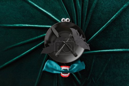 Photo for A spooky and fun plate decoration for Halloween that features a black bat with wings and eyes and a pair of vampire teeth on a green velvet background. - Royalty Free Image