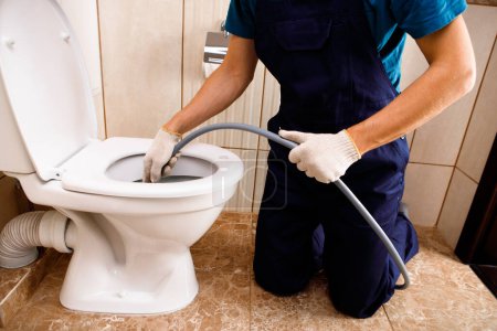 Photo for Plumber unclogging blocked toilet with hydro jetting at home bathroom. sewer cleaning service - Royalty Free Image