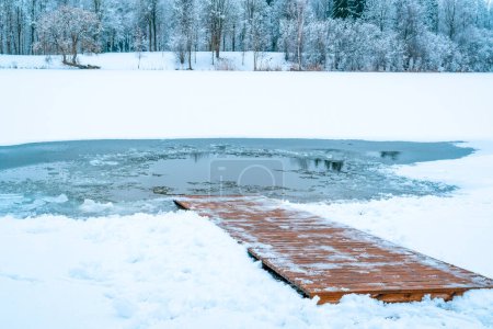 Ein Eisloch auf einem zugefrorenen See mit einem schneebedeckten Holzweg, der ins Wasser absteigt..