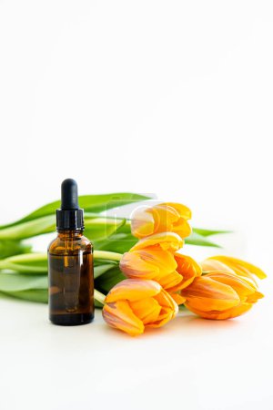 Photo for Amber glass cosmetic dropper bottle and orange tulip flowers isolated on white background, serum bottle mockup, design-ready beauty product container - Royalty Free Image