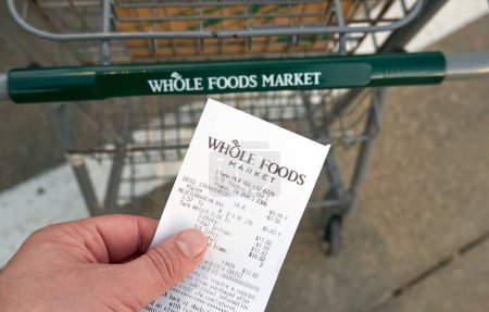 Foto de Dallas TX, Estados Unidos - 25 de febrero de 2024: Una mano sosteniendo el recibo del Whole Foods Market. Propiedad de Amazon, Whole Foods una cadena de supermercados estadounidense vende alimentos libres de ingredientes artificiales y grasas poco saludables. - Imagen libre de derechos