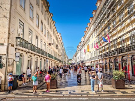 Foto de Lisboa, Portugal - 27 de agosto de 2023: Personas caminando por la calle Augusta. La calle peatonal está pavimentada con los diseños tradicionales de adoquines y está llena de restaurantes, cafeterías y tiendas.. - Imagen libre de derechos