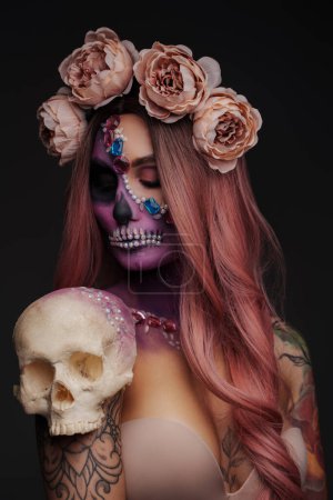 Studio shot of spooky female model with makeup and skull head against dark background.