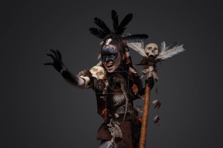 Aufnahme eines schreienden dunklen Zauberers in Aborigine-Kleidung vor grauem Hintergrund.