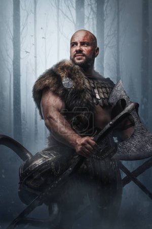 Studio shot of bald viking warrior with fur holding two huge axes in frost wood.