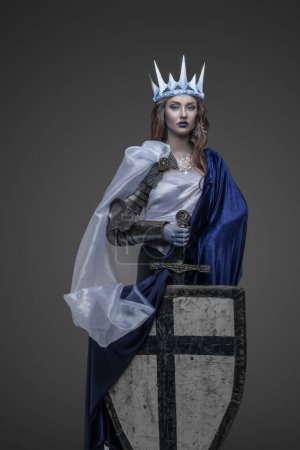 Shot of warlike ice queen with sword and shield dressed in cloak and crown.
