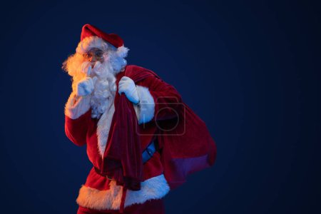 Photo for Studio shot of santa dressed in red clothes carrying bag against dark background. - Royalty Free Image