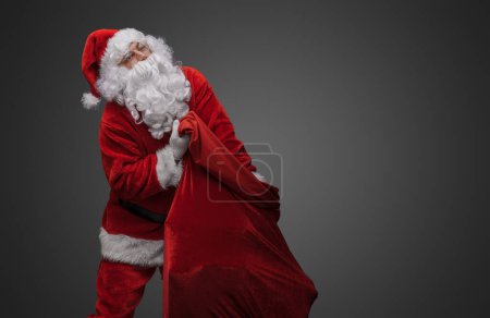 Photo for Portrait of xmas santa claus with beard carrying bag isolated on grey. - Royalty Free Image