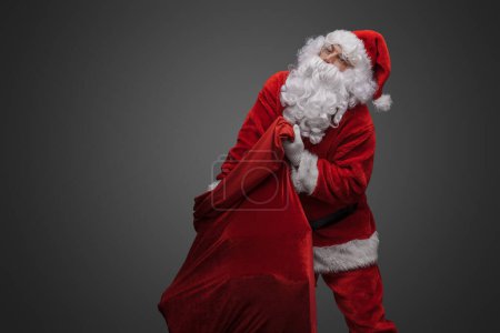 Photo for Portrait of xmas santa claus with beard carrying bag isolated on grey. - Royalty Free Image
