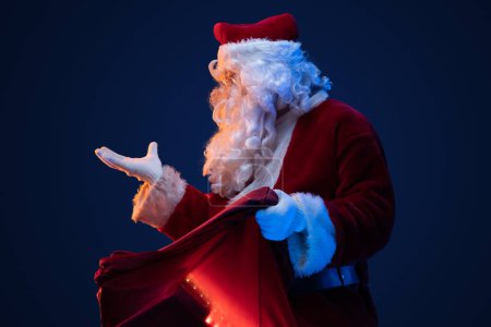 Photo for Studio shot of surprised santa with bag and long beard looking away. - Royalty Free Image