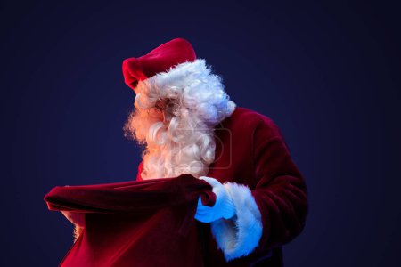 Foto de Retrato de Papá Noel viejo con gafas y bolsa con regalos sobre fondo oscuro. - Imagen libre de derechos