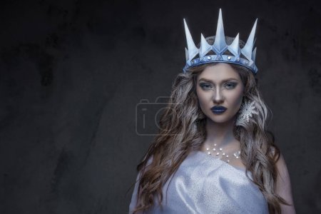 Porträt einer attraktiven Eiskönigin mit lockigem Haar und gefrorener Haut, die in die Kamera starrt.