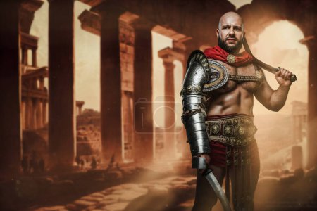 Téléchargez les photos : Portrait de gladiateur antique avec torse nu posant avec des épées doubles sur des ruines antiques. - en image libre de droit