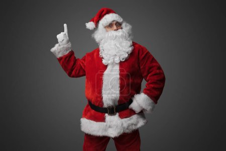 Photo for Portrait of old santa claus dressed in red suit pointing up. - Royalty Free Image