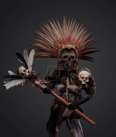 Téléchargez les photos : Photo de sorcière aztèque du passé avec coiffe à plumes et masque tenant le personnel avec tête de crâne. - en image libre de droit